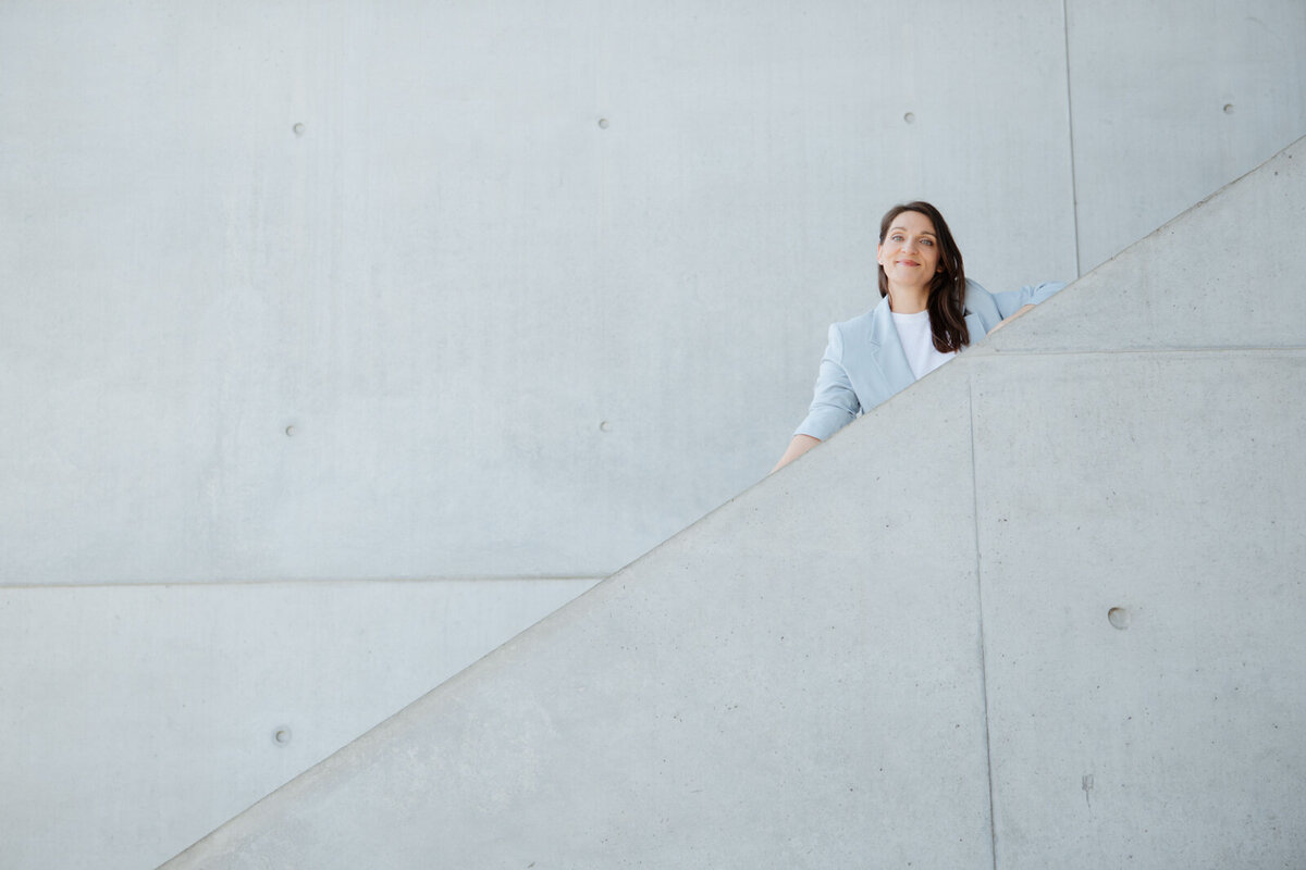 Stephanie Bretz – Detailaufnahme, minimalistisches Porträt mit architektonischem Setting auf Treppe.