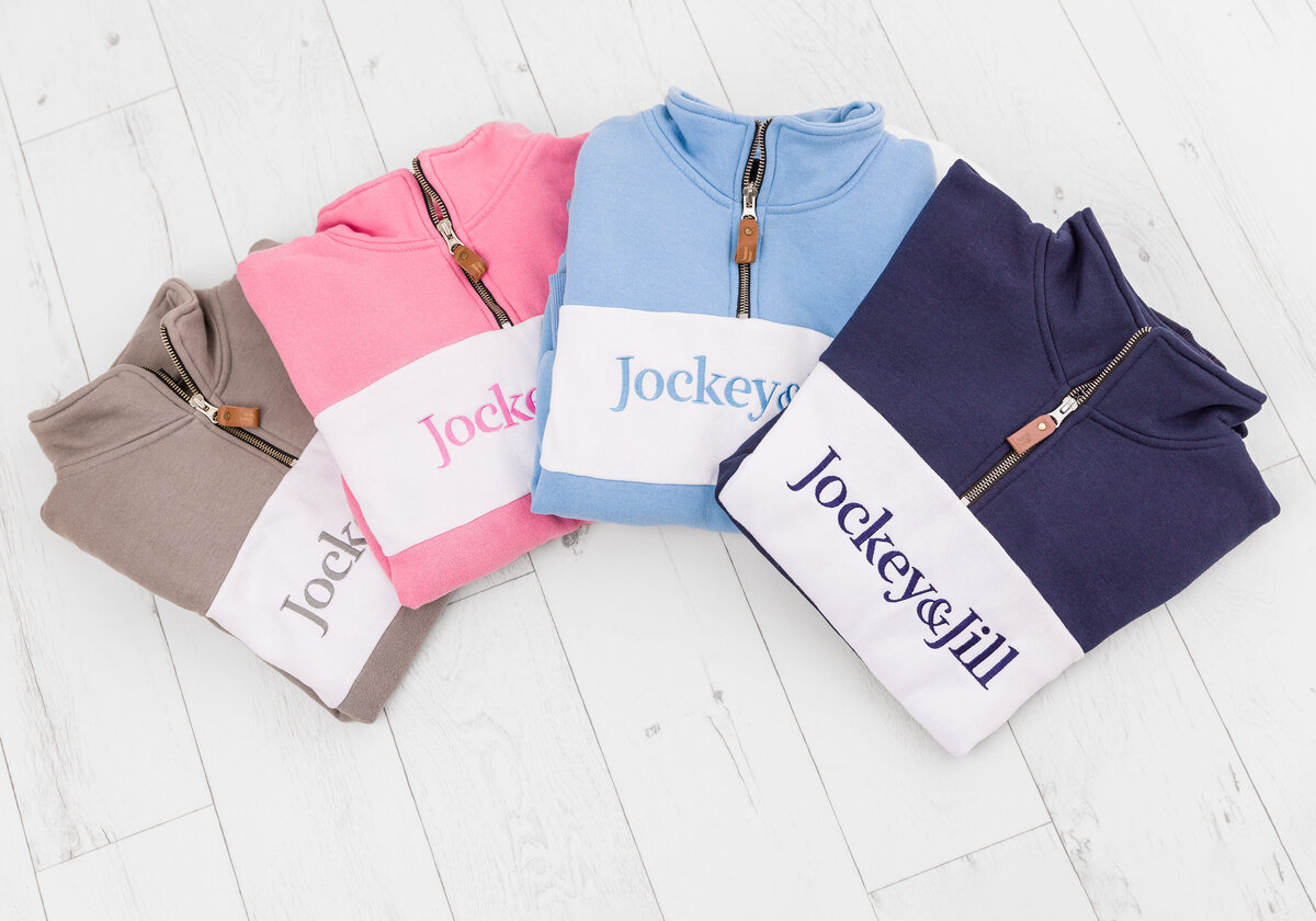 Product shots for Jockey&Jill. Taken in studio by photographer Claire Howes, Norwich. The image is a of four 3/4 zip riding jumpers laid out flat lay on a white wooden floor.