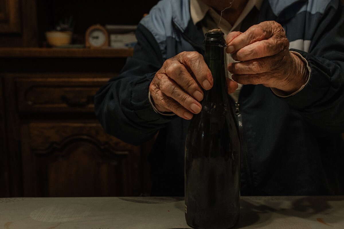 Photograph of an elderly man opening his last bottle of homemade cider, part of The Quiet Gift series by Marie Kenny.