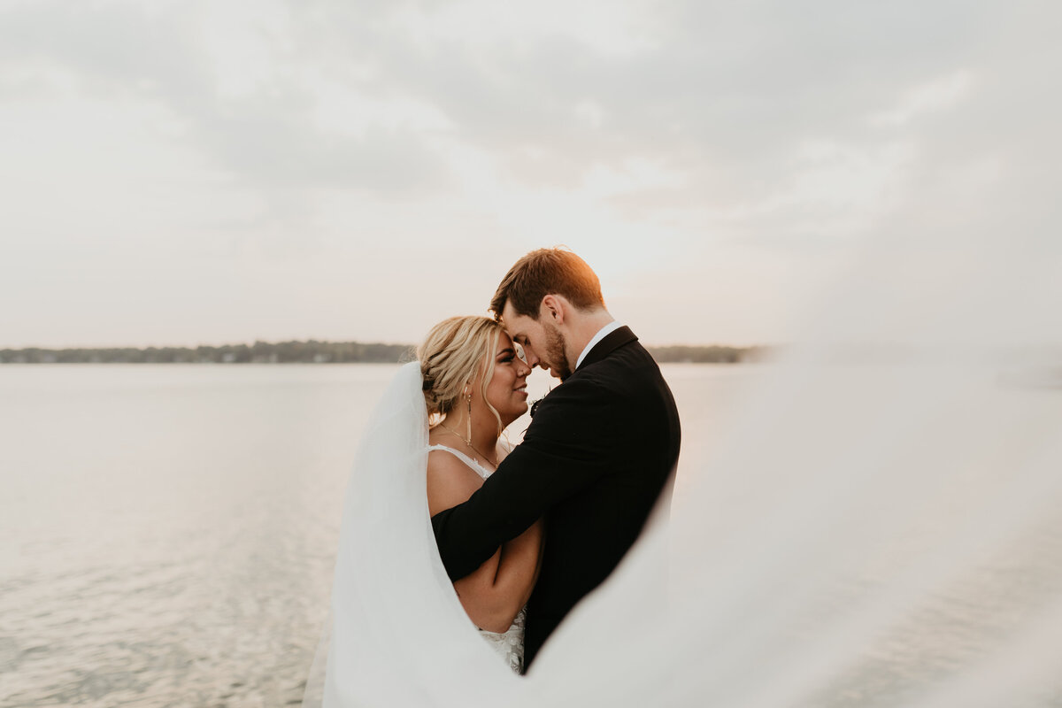 bride and groom with sweeping veil overlooking a lake at sunset