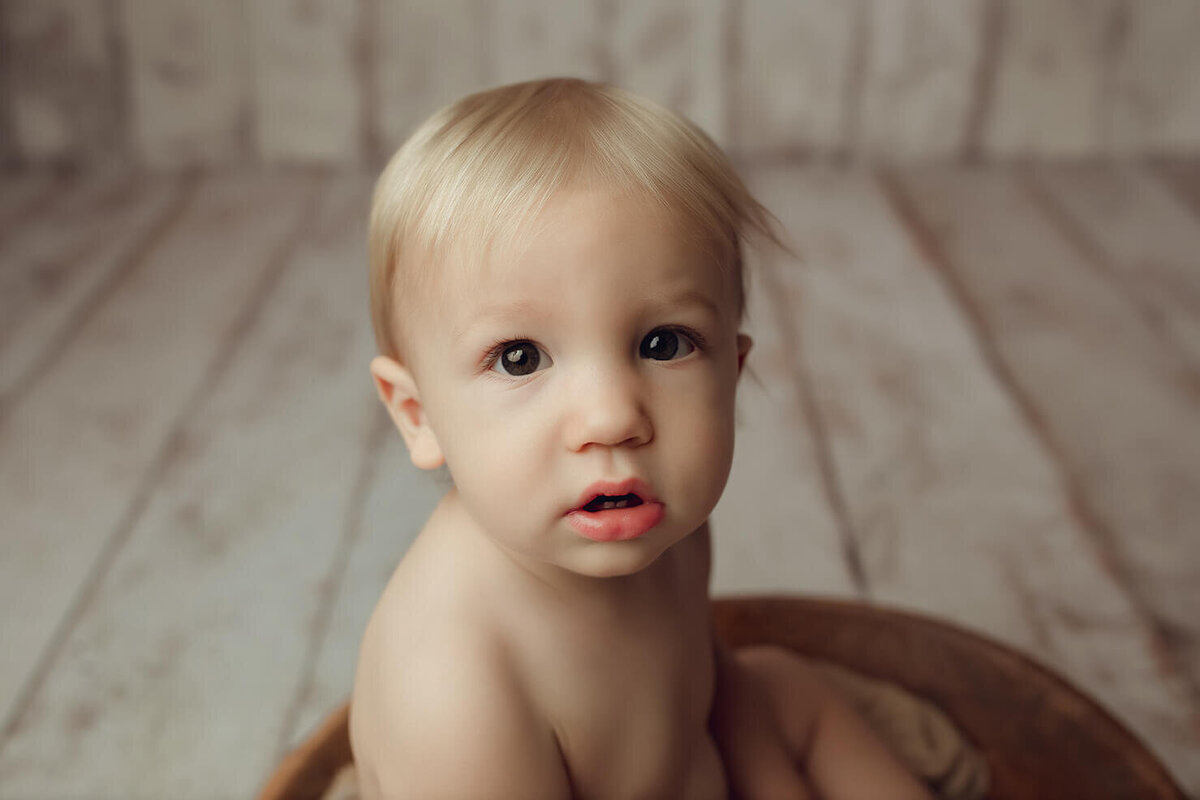a one year old boy sitting on a wood backdrop close up