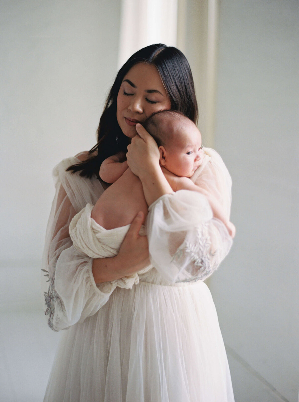 Mother holding newborn against neutral backdrop, Bay Area newborn photographer session.