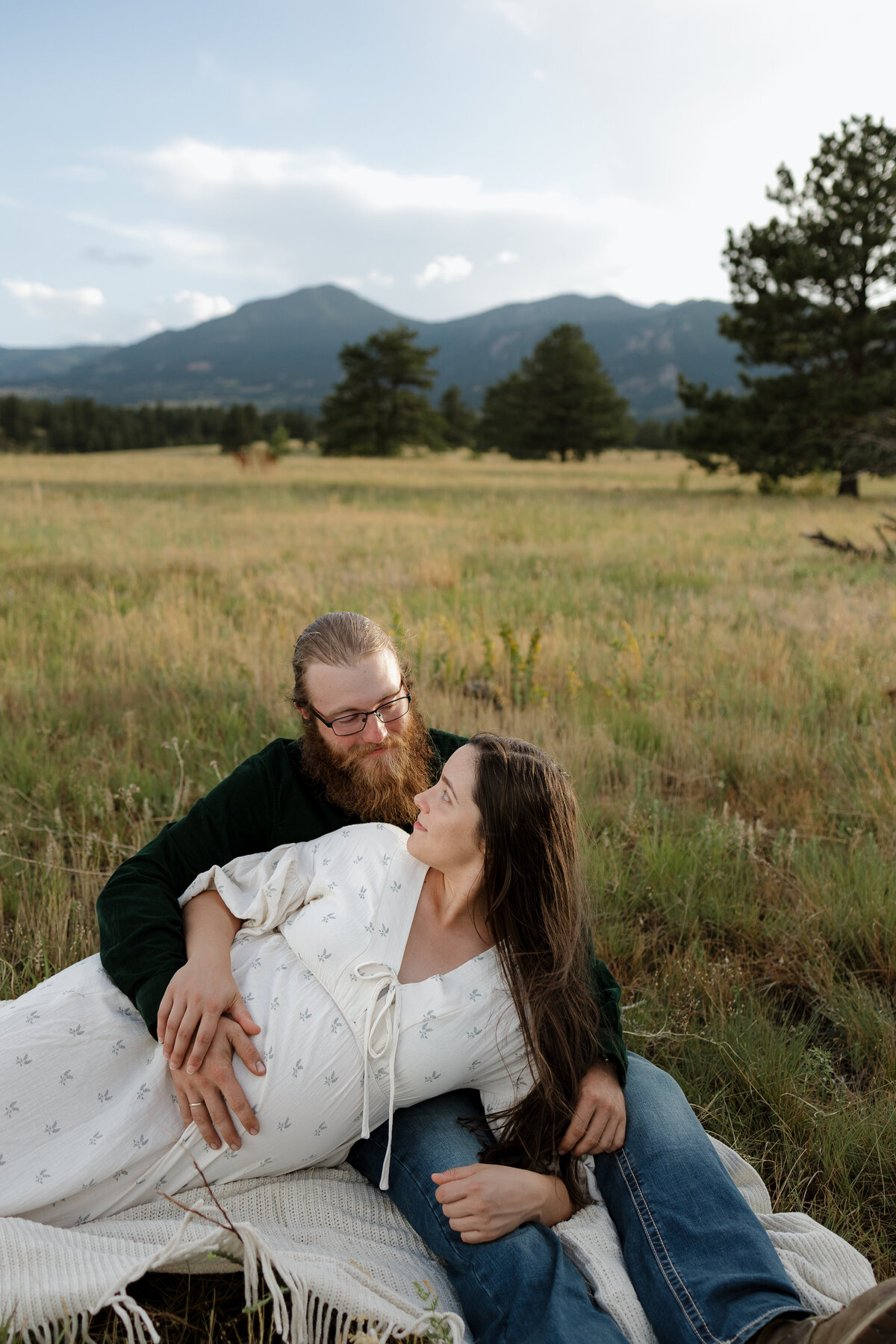 expectant parents leaning on each other while sitting on the ground caressing belly while looking at each other and smiling during lifestyle maternity session with Alexis Adkins Photography in Boulder Colorado