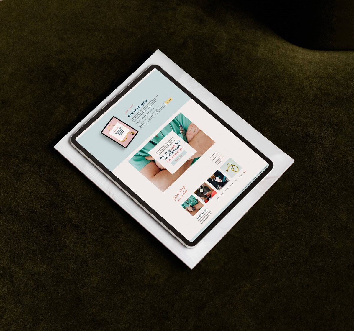 A tablet displaying a webpage with an image of a person, text, and product thumbnails rests on a magazine atop a dark green surface, showcasing showit web design for personal brands.