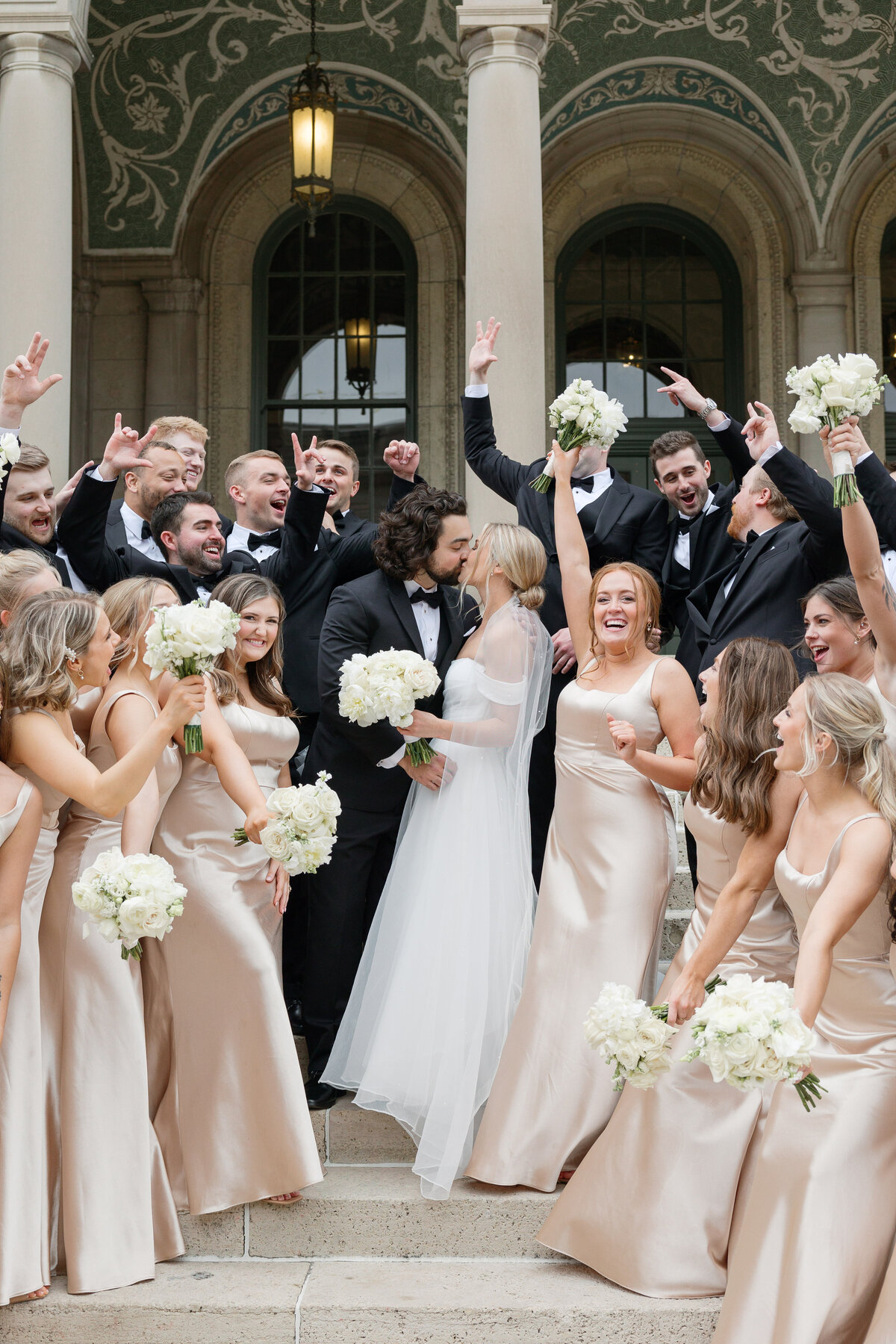 The wedding party cheers joyfully on the iconic steps of The Memorial Union in Madison, capturing the excitement and love shared on this special day.