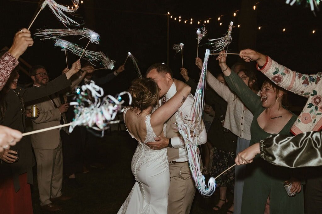 Bride and groom share a kiss beneath a tunnel of waving streamers as they exit their wedding reception. 