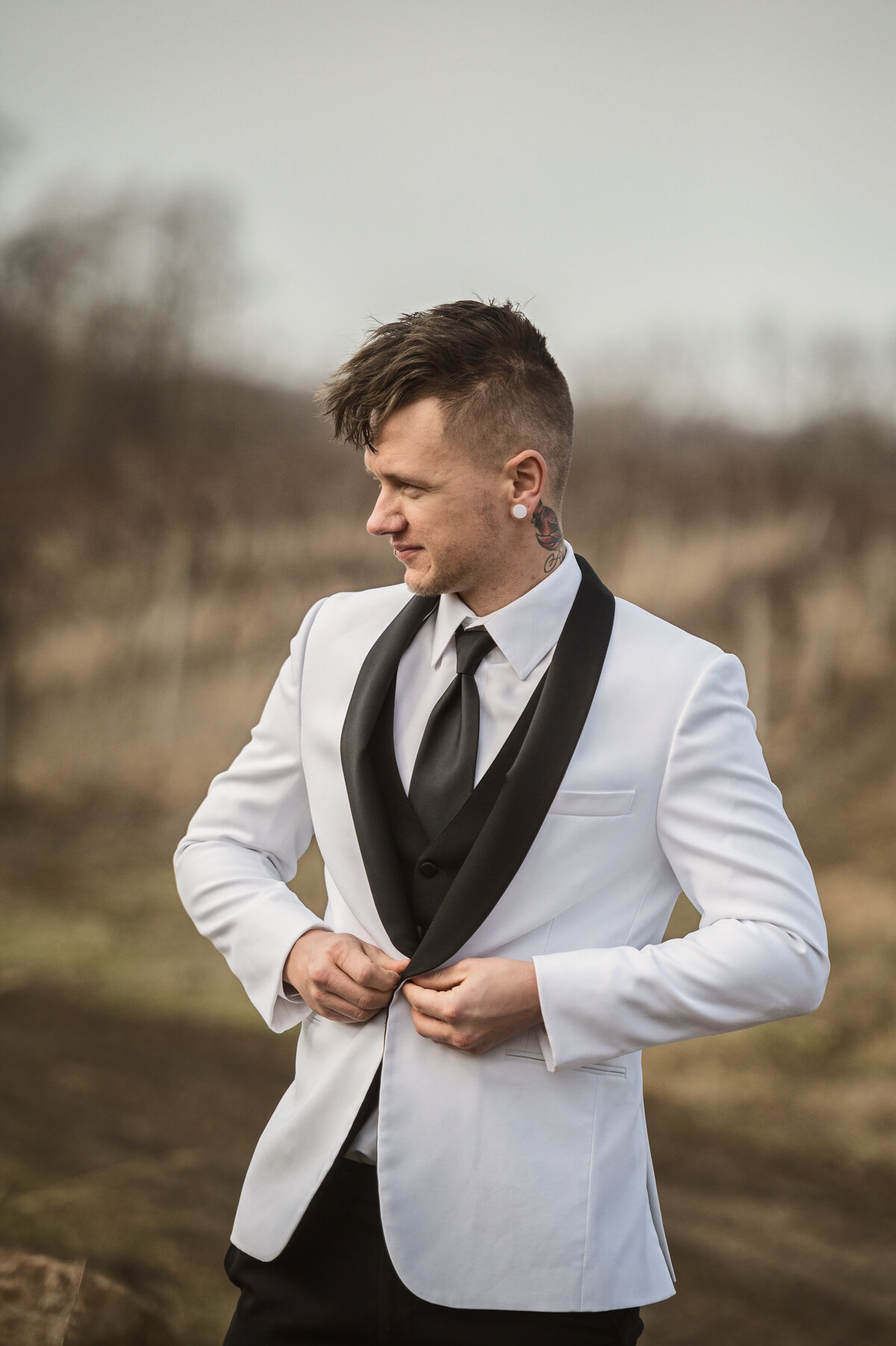 Modern groom with tattoos buttoning jacket before ceremony at Quincy Cellars in Ripley New York.