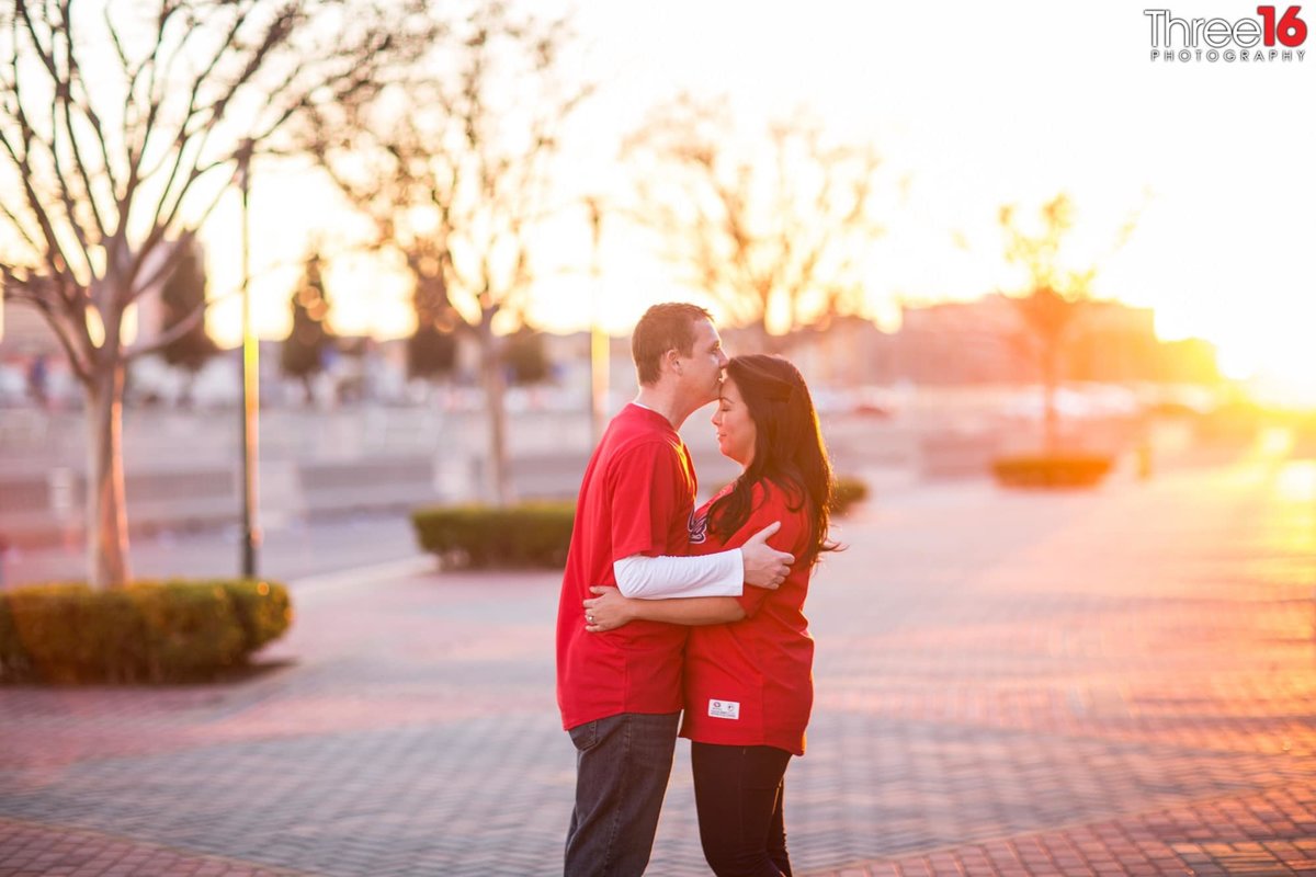 Groom-to-be kisses his girl on the forehead during sunset