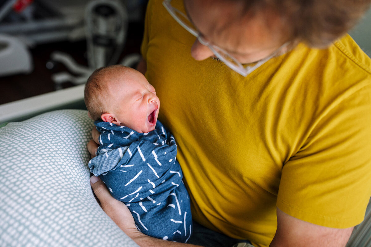 dad holding a yawning newborn in a blue patterned swaddle blanket