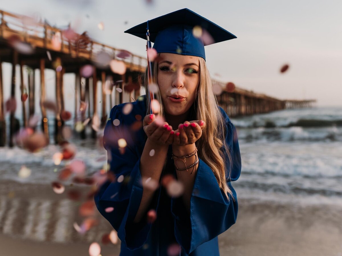senior girl celebrating graduation blowing confetti at the beach