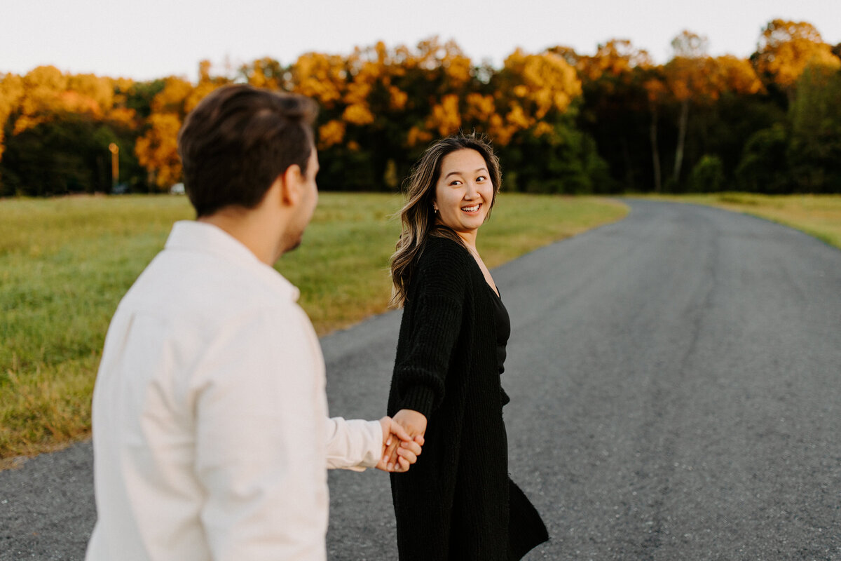 couple holding hands while walking along a small road