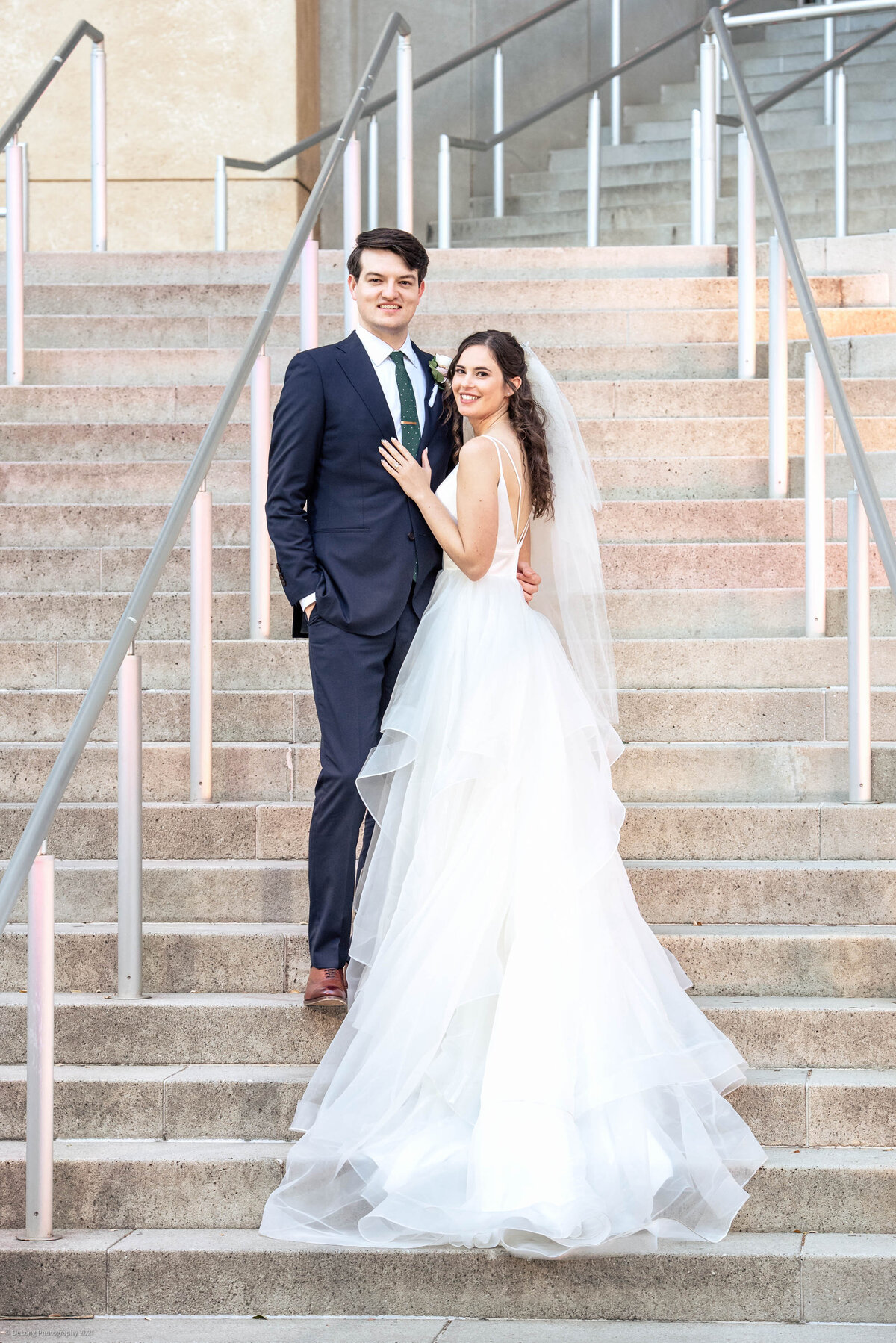 Bride turned slightly away from camera looking over her shoulder with her arms on her groom on the steps of the Mint Museum in Uptown by Charlotte wedding photographers DeLong Photography