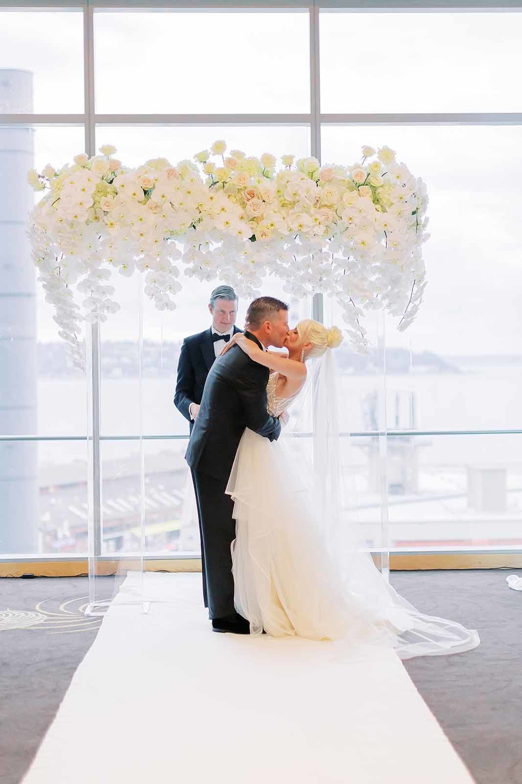 bride and groom kissing under arbor of white orchids