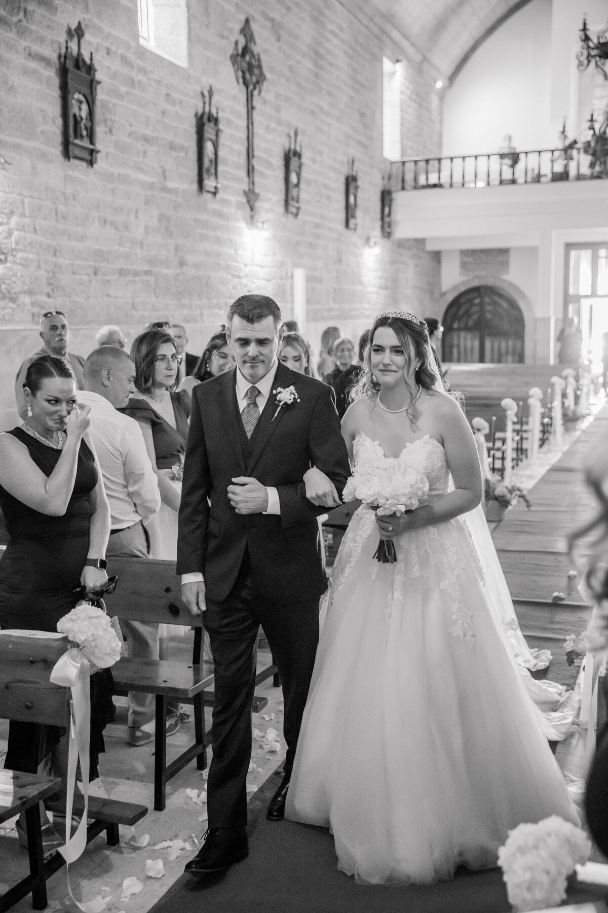 Church Wedding in Spain | A black and white image of a bride and her father walking down the aisle of Iglesia de Santa Mariña de Esteiro, a historic church on the coast of Galicia, Spain.