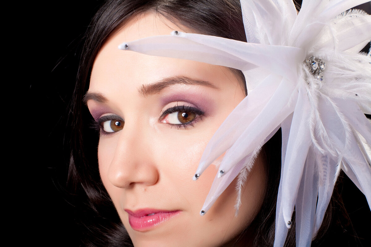 A female performer's close-up headshot of her face wearing a large white flower in her hair