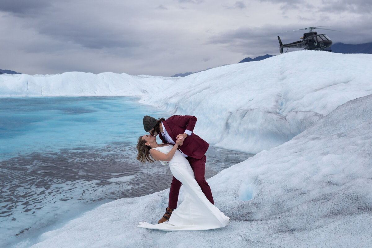 A groom dips his bride next to a glacier in Alaska.