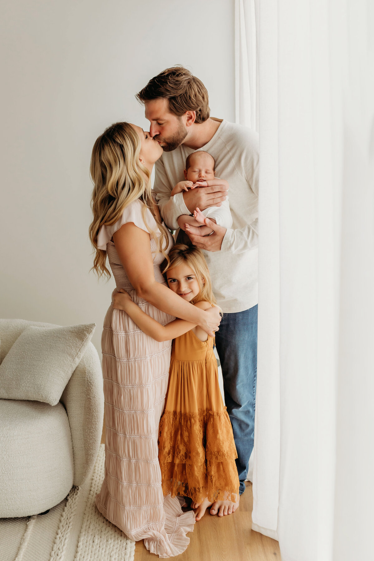 A family stands in beautiful natural light admiring their newborn baby, inside a Vancouver Washington studio