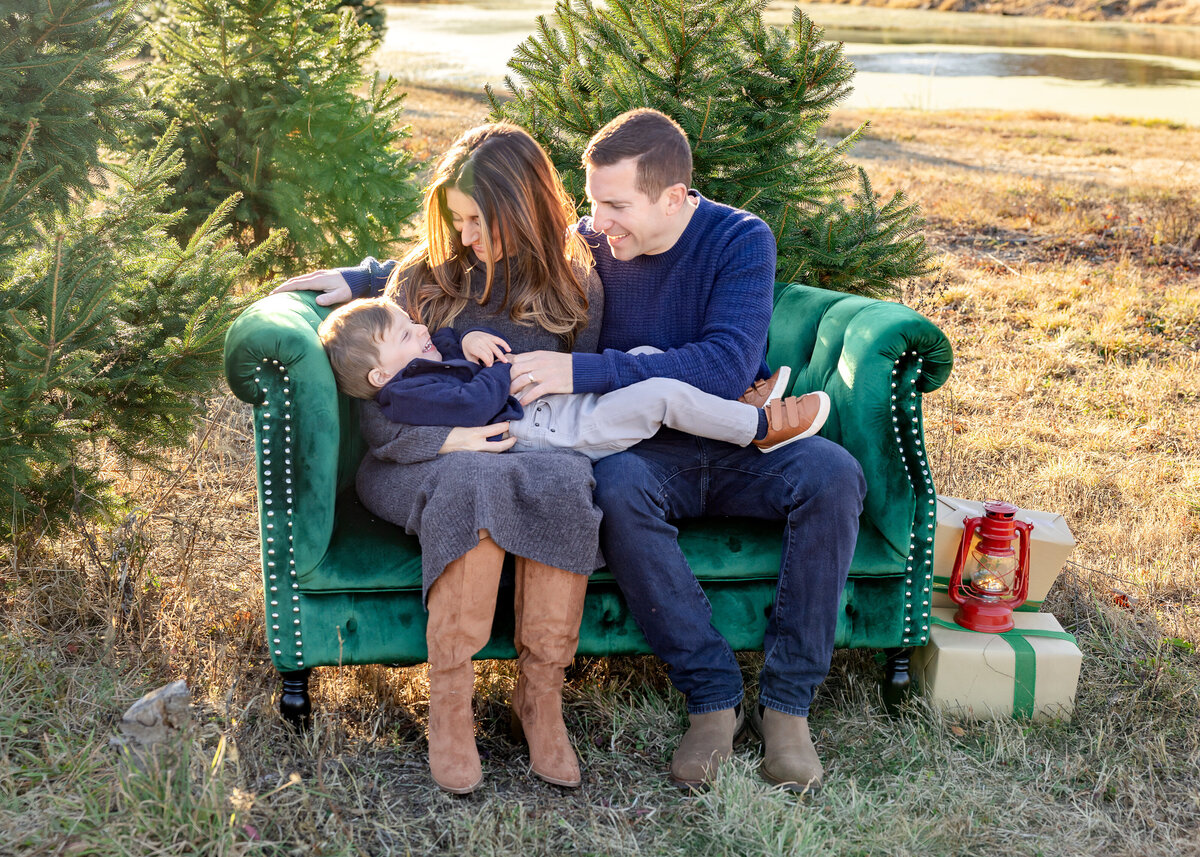 Mom and dad laughing and tickling son on a couch at a Christmas tree farm in NJ