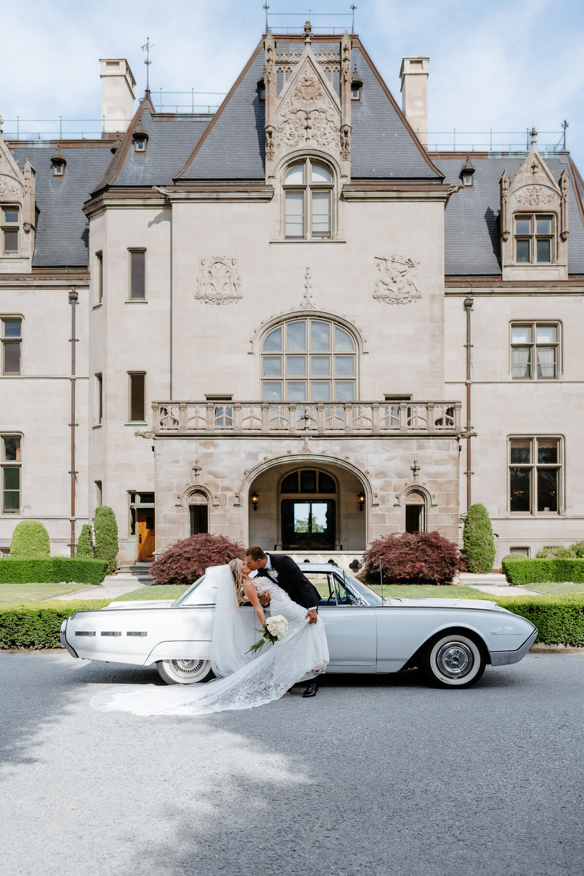bride and groom doing a dip kiss with a white vintage car in the background