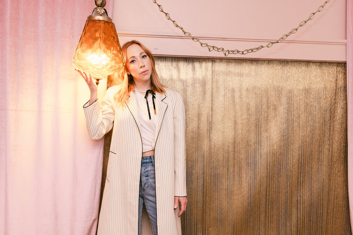 Creative branding portrait of a fashion-forward entrepreneur in a retro-inspired pink and gold studio, holding a vintage amber light for a bold editorial look.