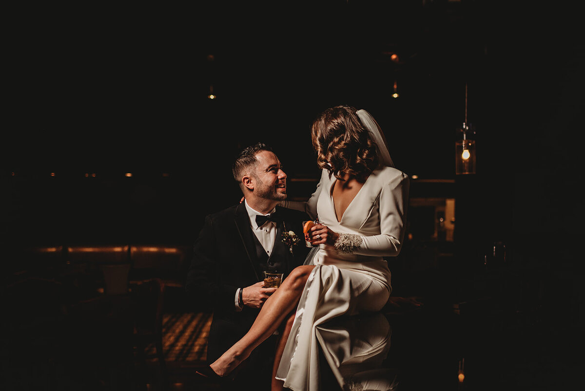 Maryland wedding photographer captures bride and groom and a luxury lounge sitting together with bride on the grooms lap as they hold cocktails for their Baltimore wedding