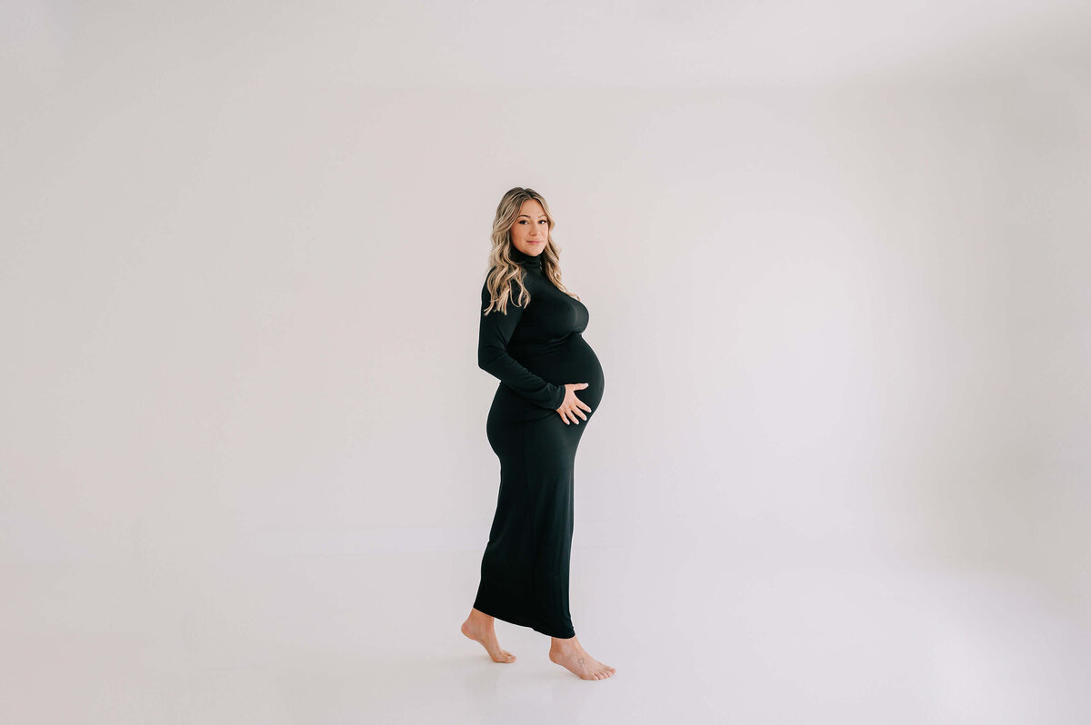 pregnant mom in black dress walking in studio during Joplin MO maternity photography session