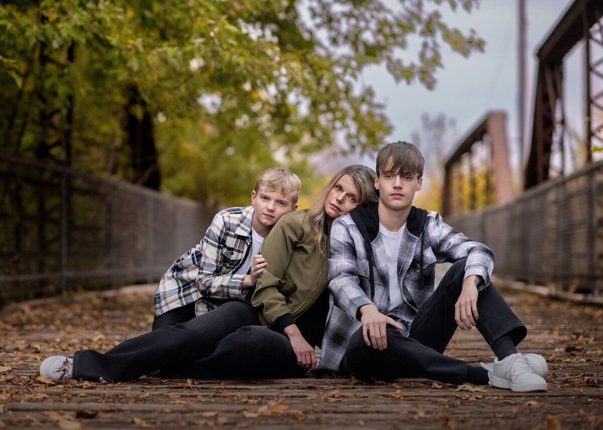 A mom and her 2 sons sit on a bridge and take family pictures