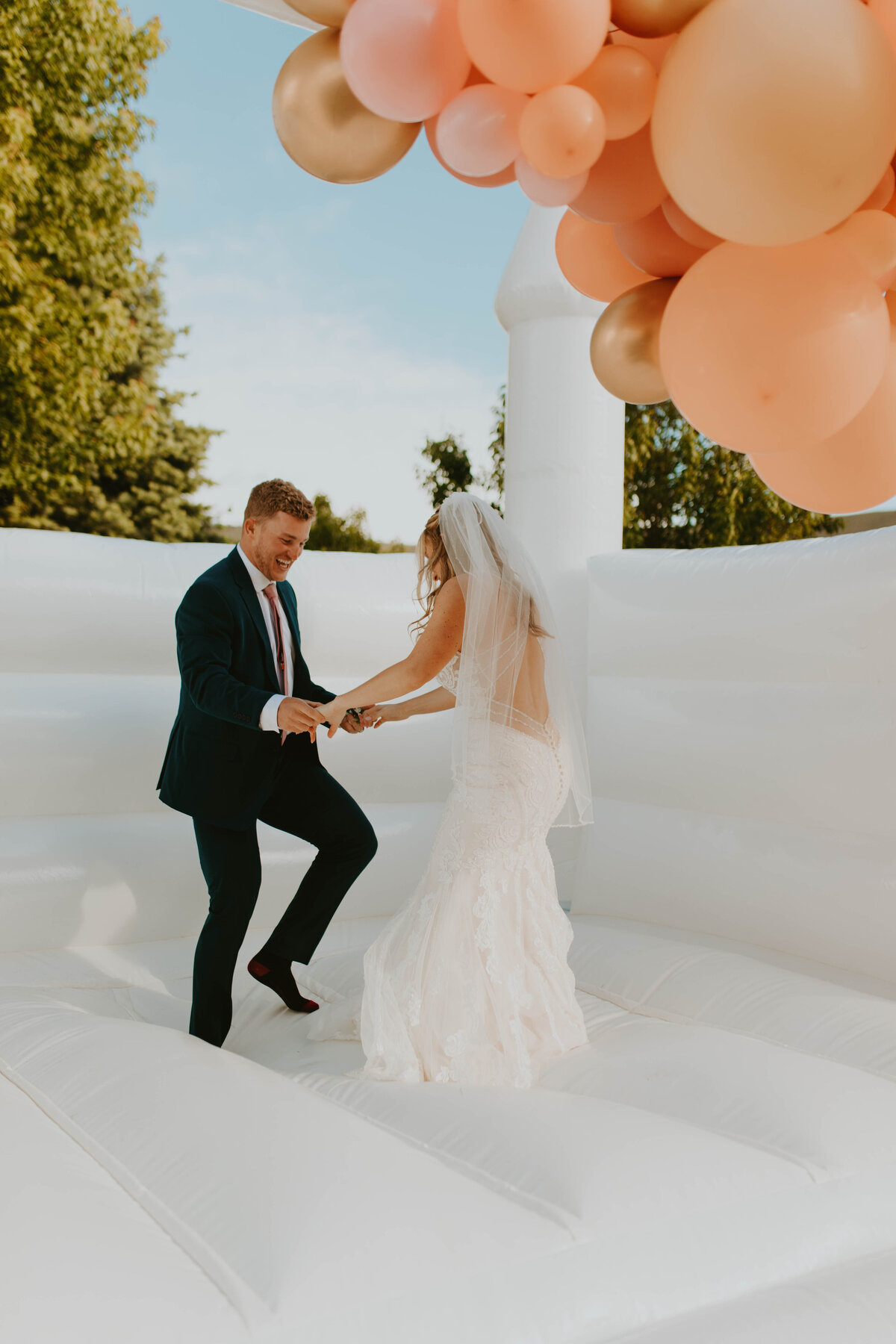 Bride and groom jumping in a white bouncy house.