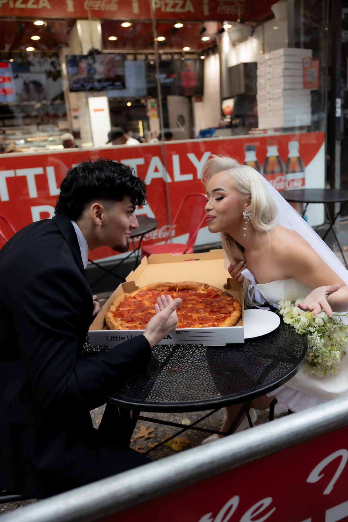Urban NYC elopement: The couple sits at a pizza shop table with pizza slices and drinks.