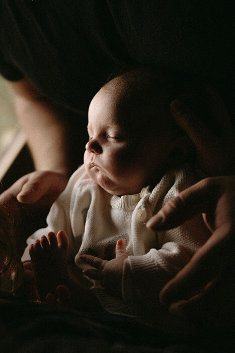Nouveau né endormi dans les bras de ses parents. Shooting photo naissance par Kamescop, photographe en Bretagne.