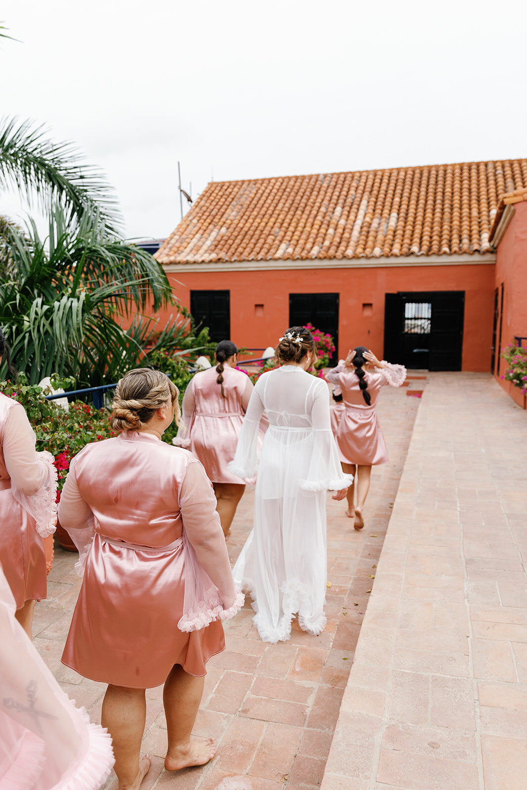 Bridesmaids in blush robes walking towards the wedding ceremony, set in a charming Cartagena Colombia courtyard.