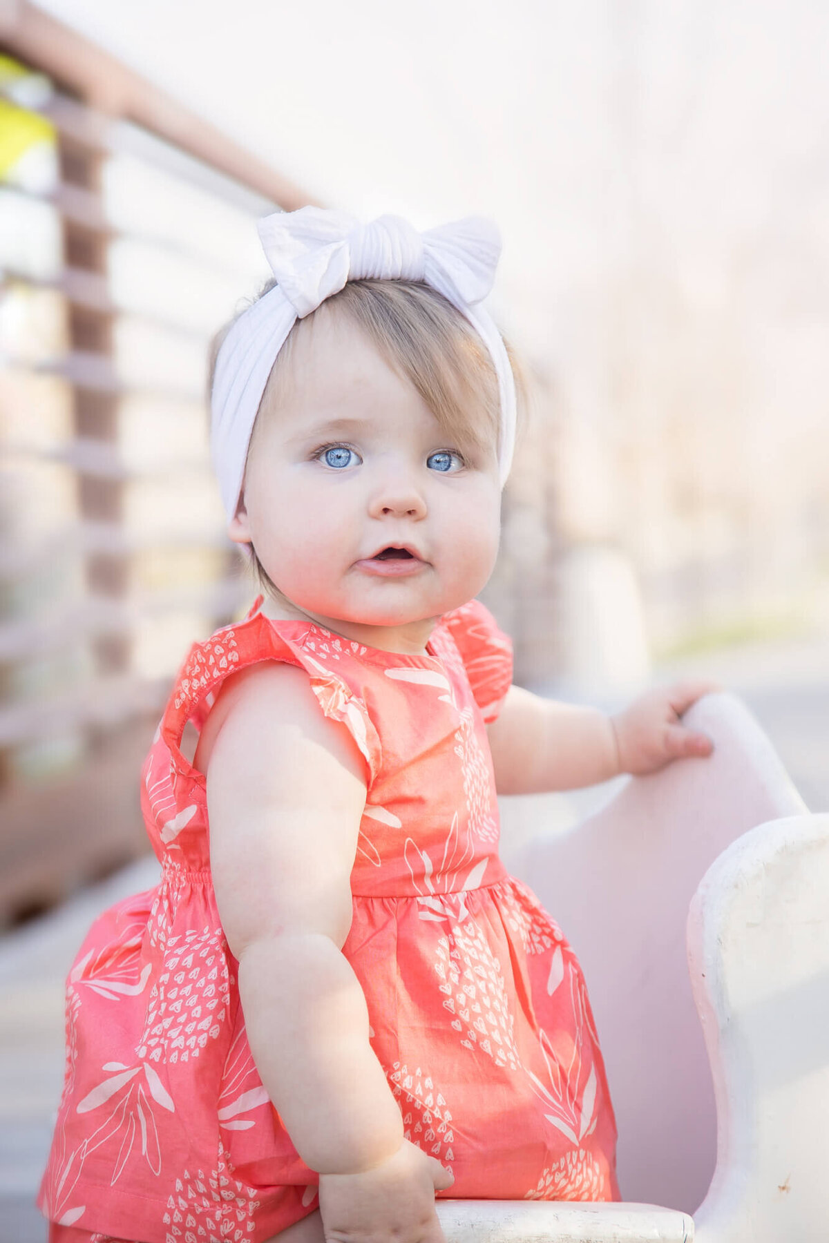 stunningly bright eyed one year old girl standing on a bridge