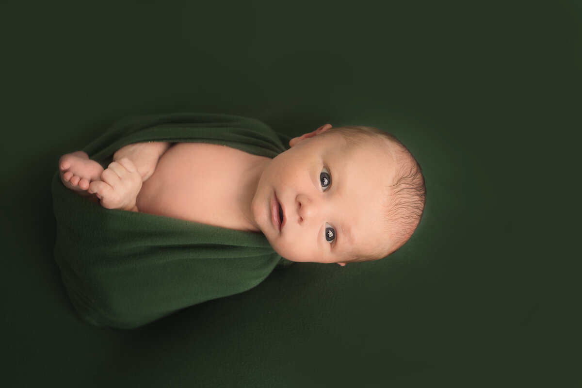 Newborn baby boy wrapped in green wrap laying on green drop during newborn photoshoot in Franklin Tennessee photography studio
