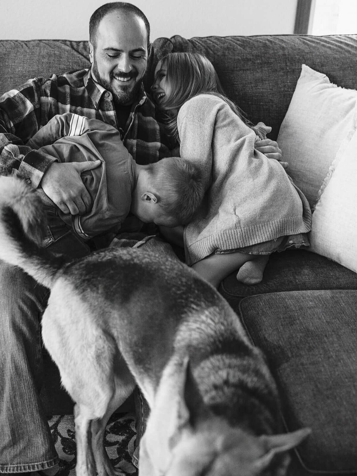A man and two children hug on a couch with a dog in the foreground.