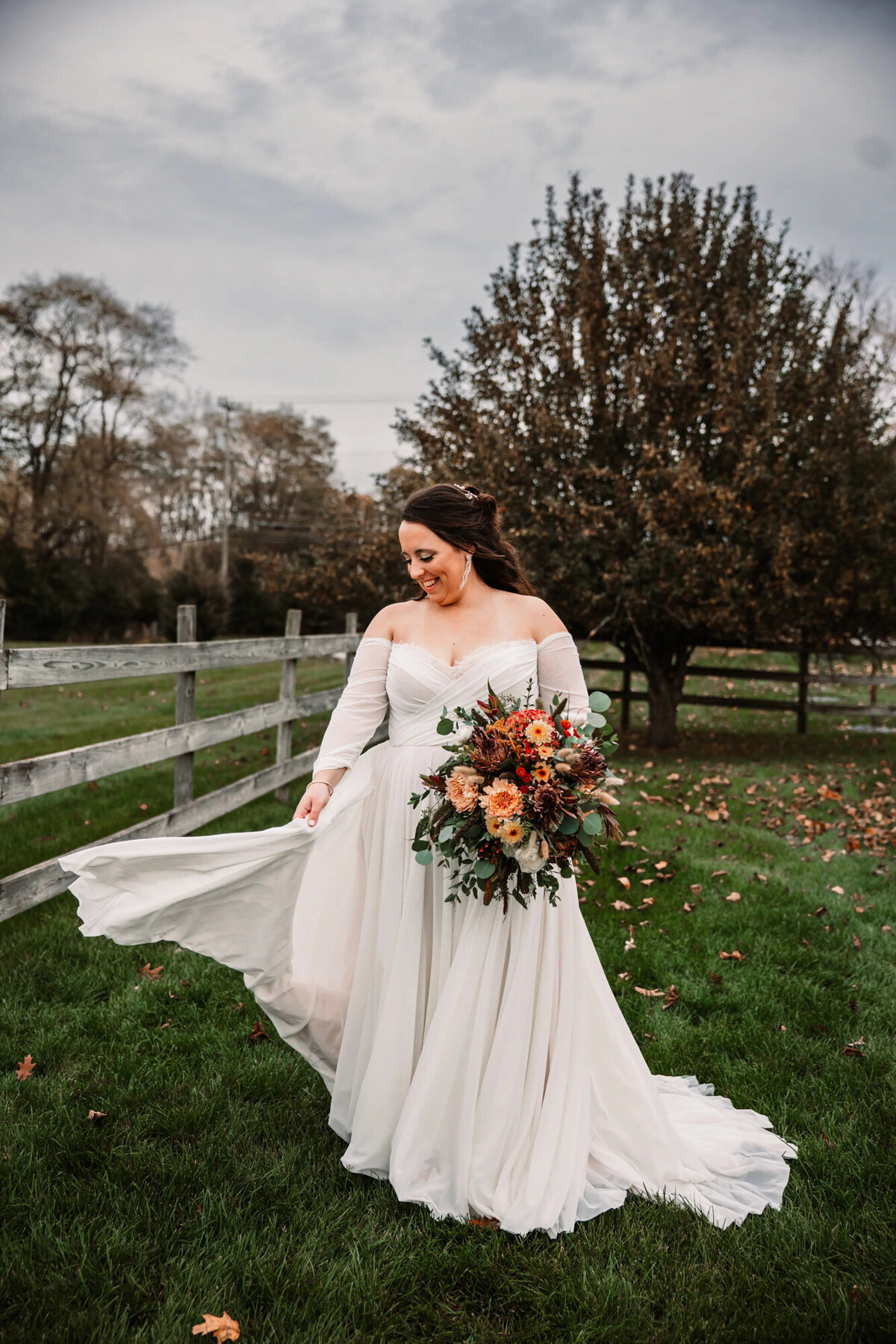 bride twirls in wedding dress while holding bouquet by a fence in a field