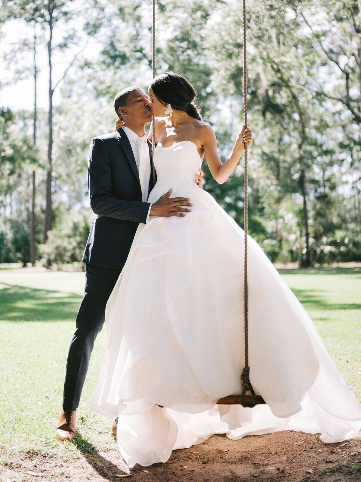The bride is standing in a swing, while kissing the groom in Montage at Palmetto Bluff. Destination wedding image by Jenny Fu Studio