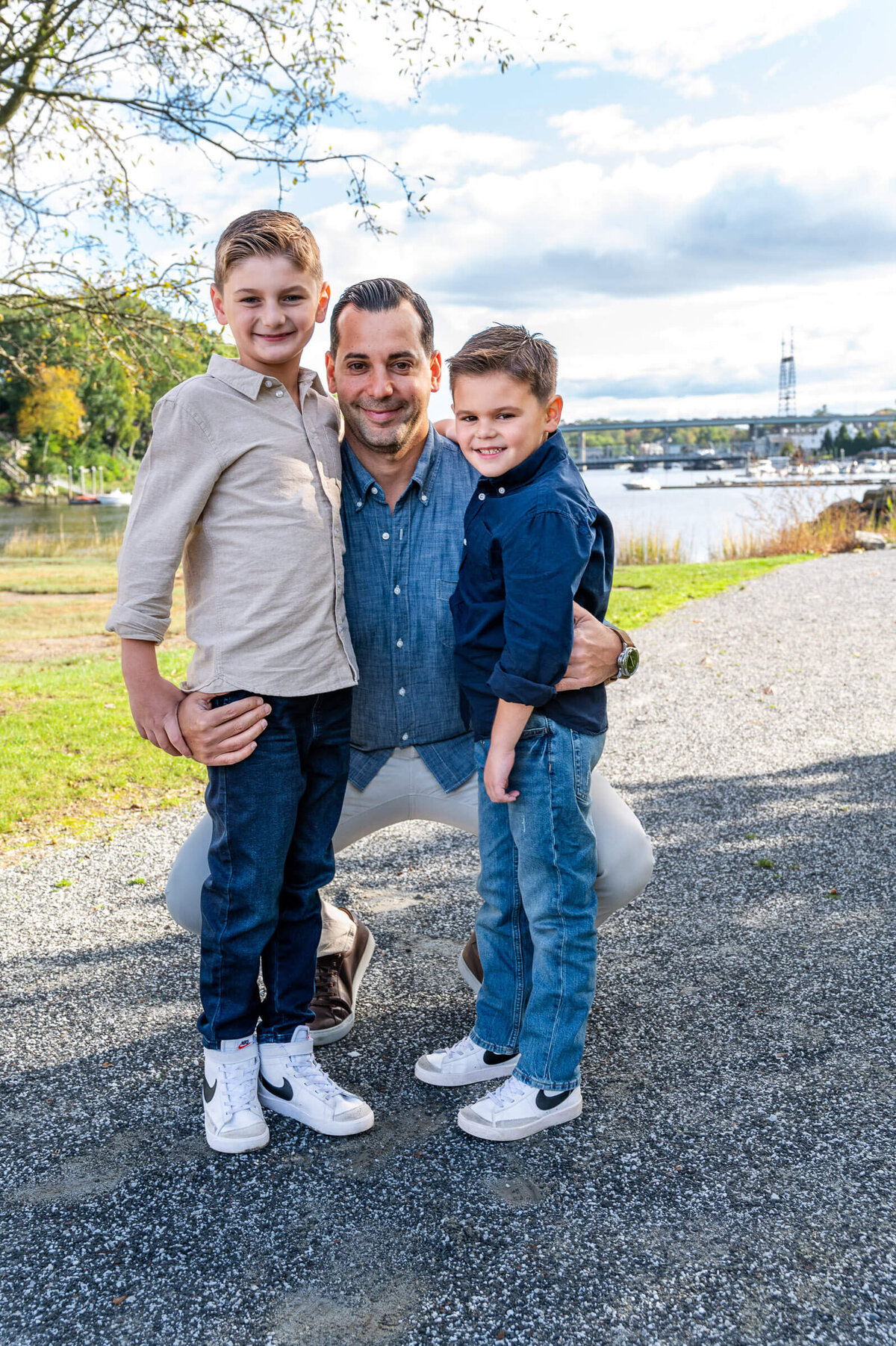 Father with this two young sons, kneeling down for a family photoshoot by the river in Westport, CT.