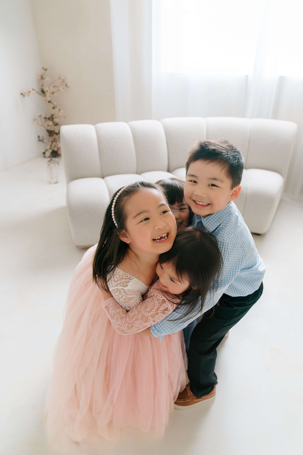 Four siblings in coordinated outfits embrace each other with big smiles during a family portrait session.