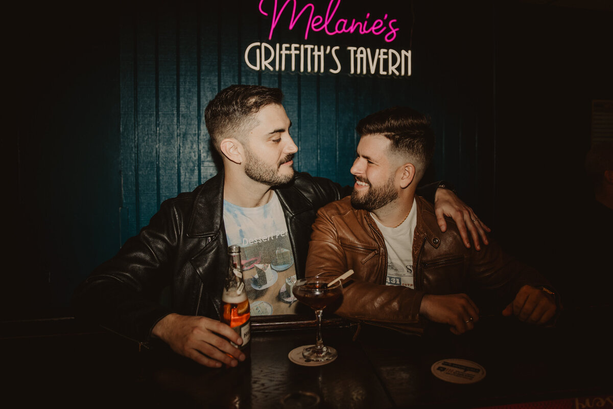 A couple sitting at a bar while one has their arm around the other 