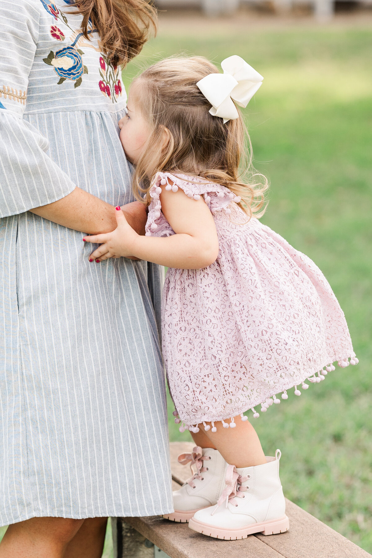 2-year-old-girl-standing-on-bench-kissing-mommys-belly