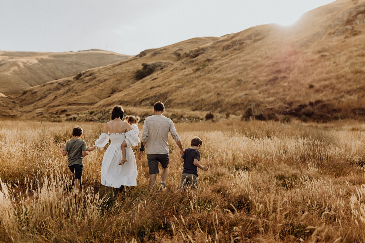 A family of five walking along a field of long grass during a family photoshoot with christchurch family photographer lucy jane