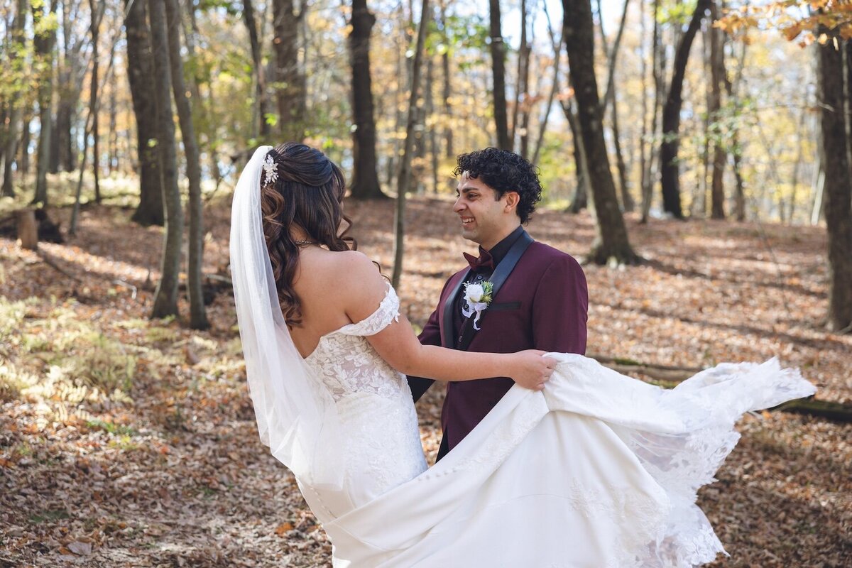 Bride twirling her dress while laughing with the groom in the woods.