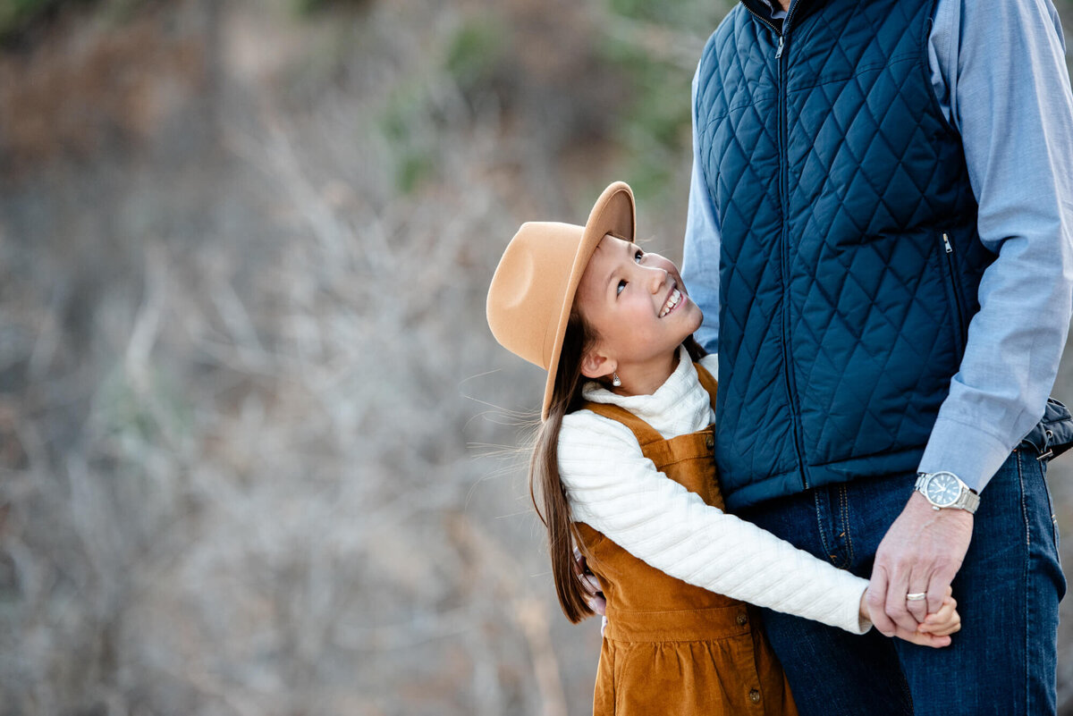 A young girl looks up to dad as she hugs him for a Denver family photographer