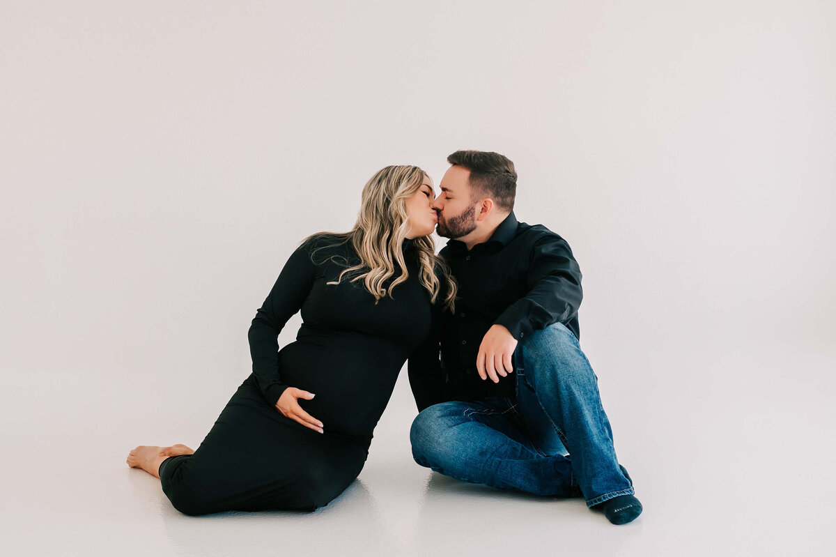 pregnant couple sitting on floor kissing enjoying their Branson Missouri maternity photography session