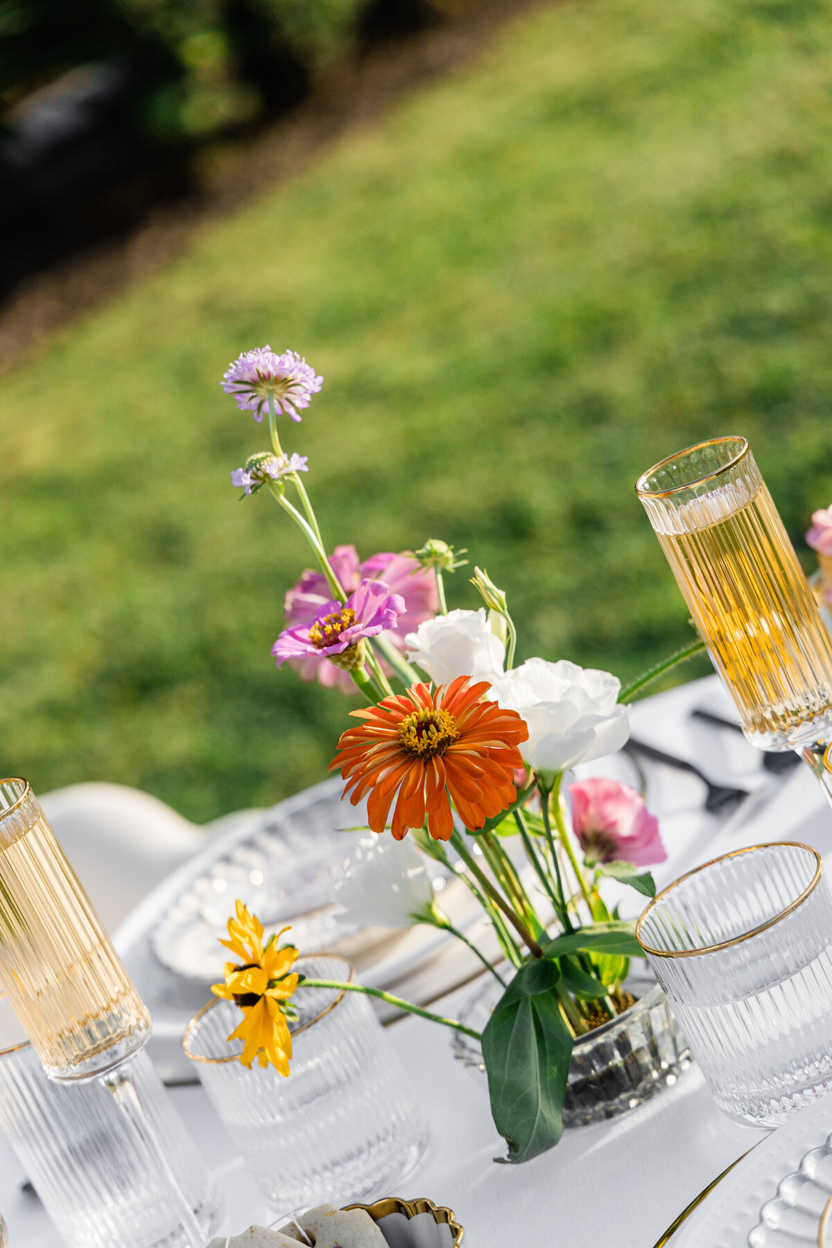 pink orange and white flowers on white table cloth with mixed metal place setting and champagne filled glass