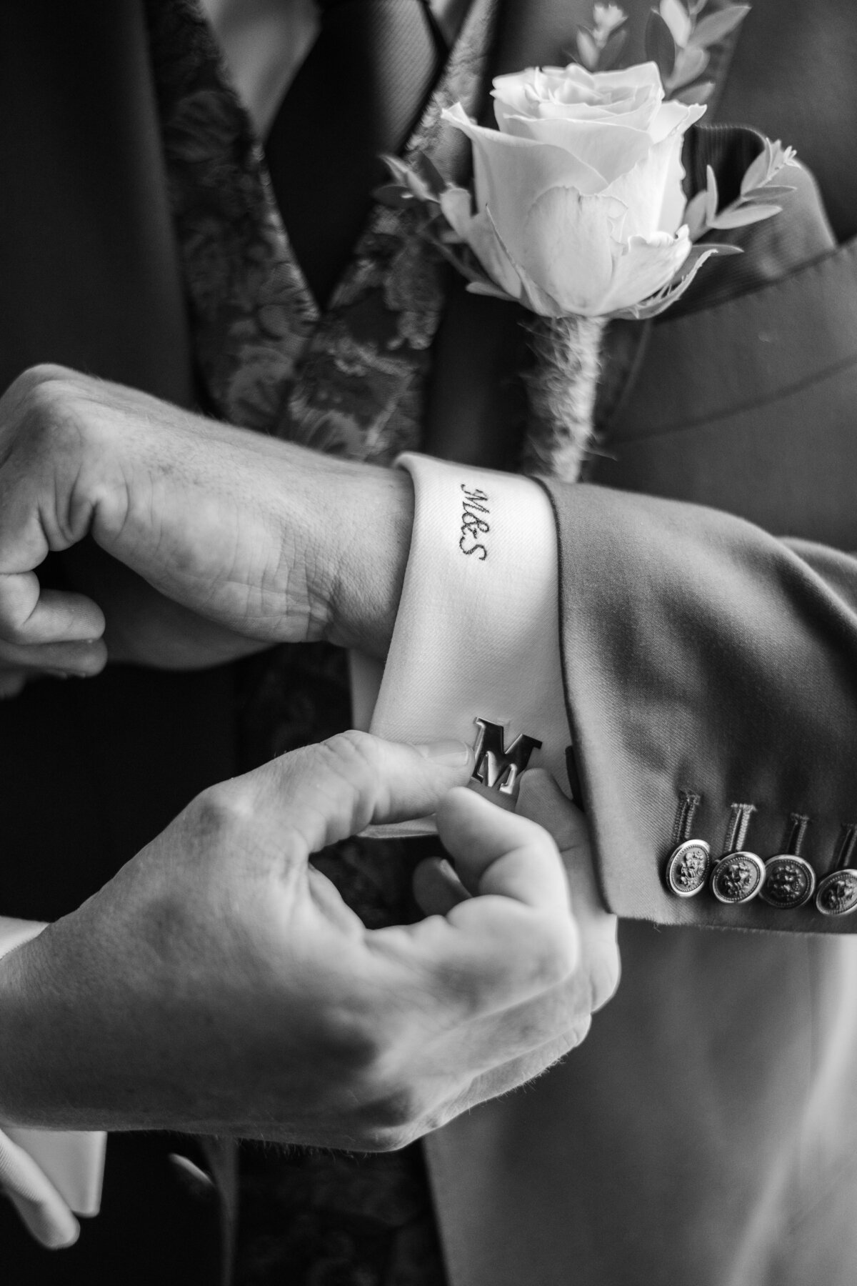 Black and white detail of a groom fixing his cufflinks in a customized suit on his wedding day