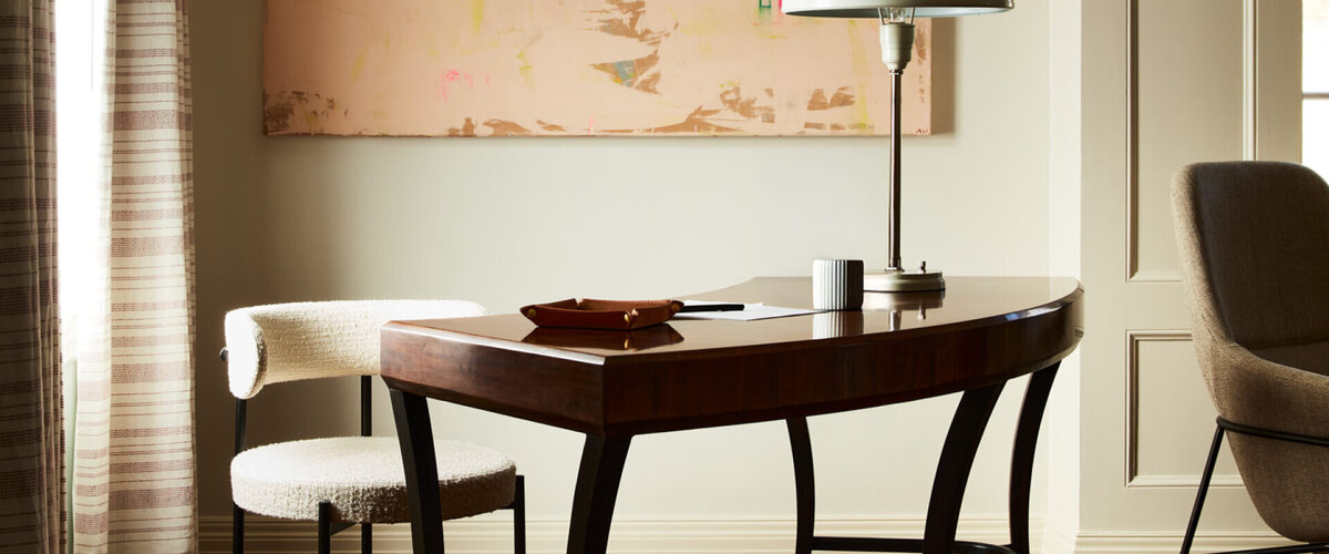 A vintage desk meets a modern chair and contemporary art, blending historic charm with a fresh perspective in this refined interior.