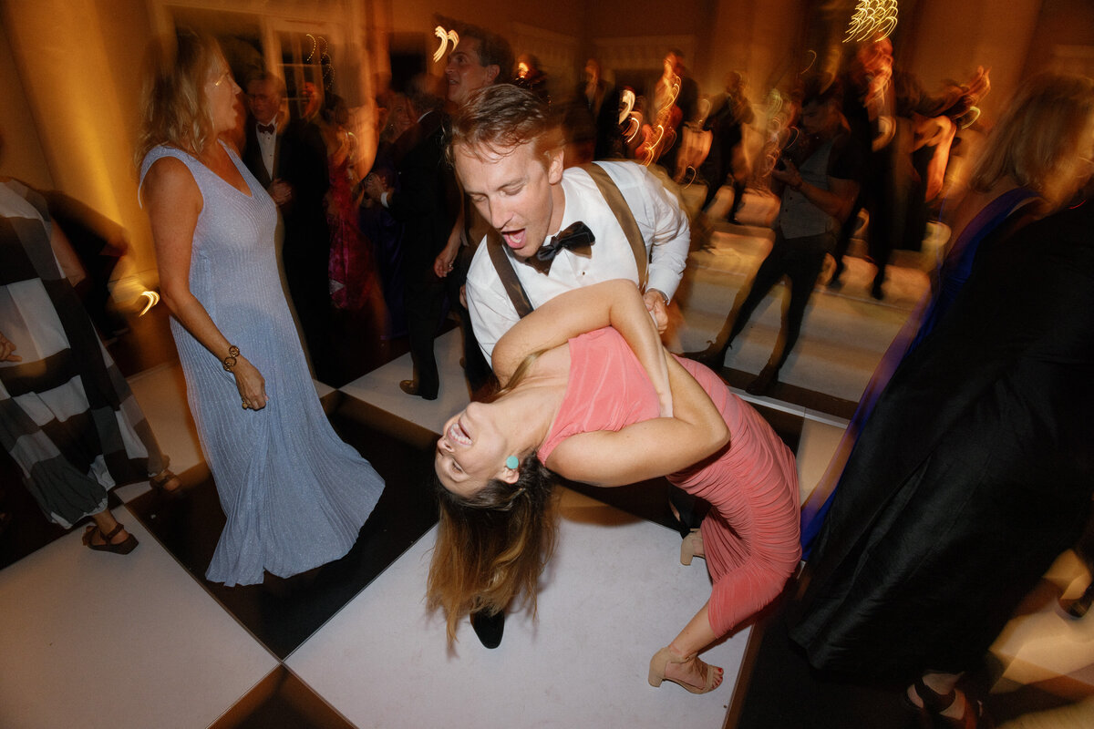 man dipping woman in orange dress on wedding reception dance floor