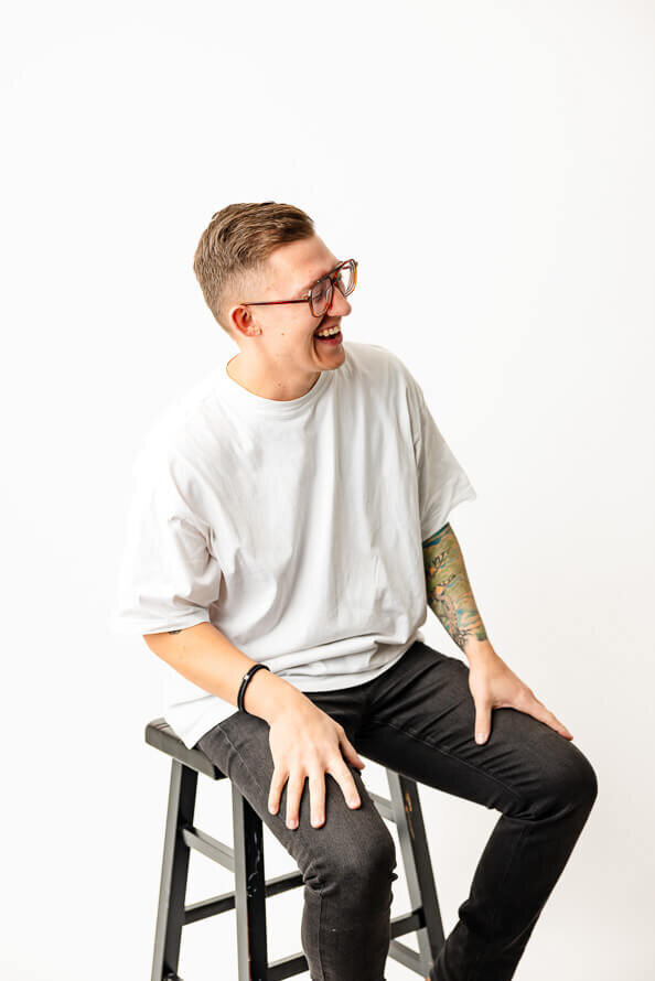 Man in white studio puts hands on legs and laughs.