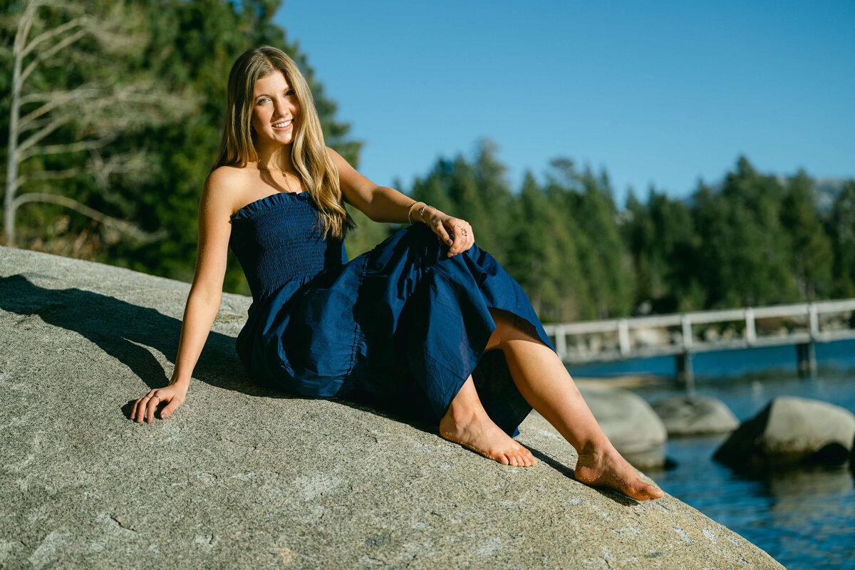Senior girl lying on a boulder on the beach in Lake Tahoe during a senior portrait session on a sunny late fall evening